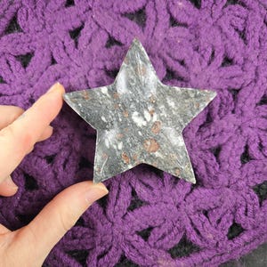 May include: A five-pointed star-shaped dish made of gray speckled stone. The dish is sitting on a purple crocheted surface.