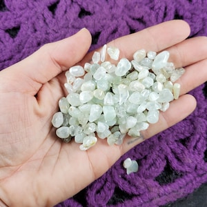 May include: A handful of small, light green aquamarine tumbled stones. The stones are smooth and polished, and they have a translucent appearance.