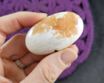 May include: A smooth, white and orange polished stone with a unique pattern. The stone is oval shaped and has a natural, organic look.