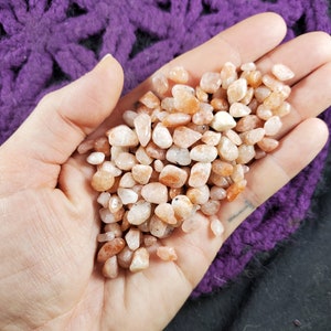 May include: A handful of small, smooth, orange and white sunstone chips. The stones are tumbled and have a natural, earthy look.