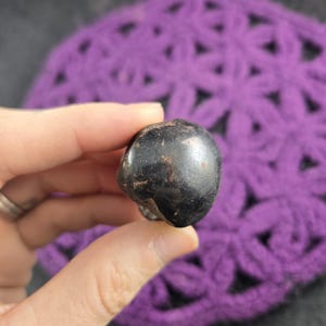 May include: A white ceramic mug with a black handle and the text "But First, Coffee" in a bold, black font. The mug is set against a blurred background, suggesting a cozy setting.