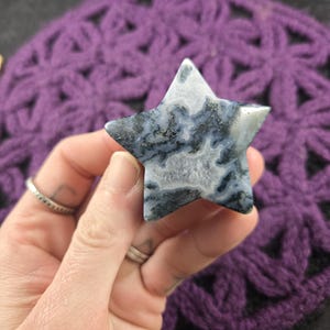 May include: A white and grey agate star with black dendritic inclusions. The star is carved from a natural stone and has a smooth, polished finish.
