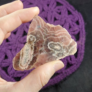 May include: A pink and gray banded agate crystal with a layered pattern. The crystal is translucent and has a smooth, polished surface.