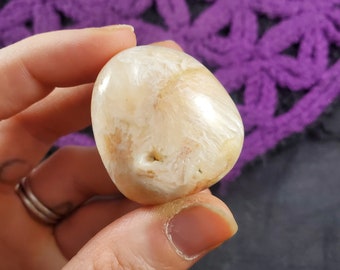 May include: A smooth, white, and iridescent crystal with a natural, organic shape. The crystal has a subtle, warm, peachy hue.