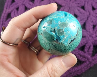 May include: A green and blue sphere of polished turquoise with a marbled pattern. The sphere is about the size of a golf ball.