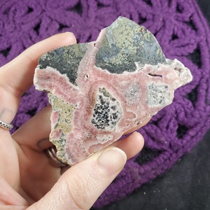 May include: A pink and gray crystal with a swirling pattern. The crystal has a rough, natural texture.