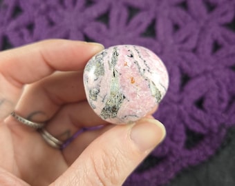 May include: A pink and gray tumbled stone with a swirling pattern. The stone is smooth and polished.