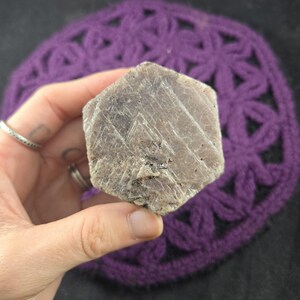 May include: A rough, hexagonal, gray-brown gemstone with striations on its surface.