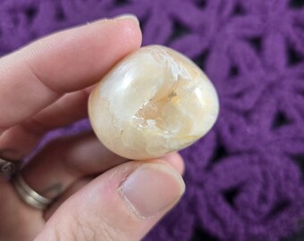 May include: A smooth, white and yellow agate crystal with a polished finish. The crystal has a translucent appearance with white and yellow swirls and patterns.