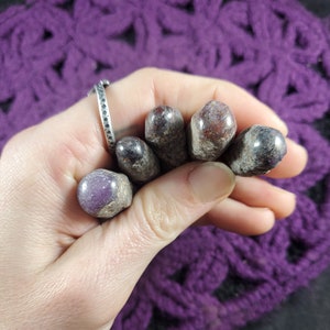 May include: Five tumbled stones with a purple and red color variation. The stones are smooth and polished.