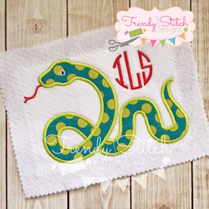 May include: A white felt applique with a green snake with yellow polka dots and a red tongue. The snake is curled up in a circle. The letters "ILS" are embroidered in red in a circle above the snake.
