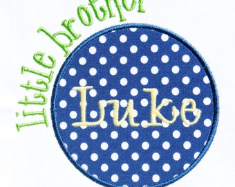 May include: A blue and white polka dot circle with a yellow embroidered name "Luke" inside. The circle is surrounded by a green embroidered phrase "little brother".