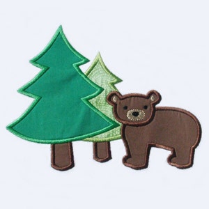 May include: An embroidered design featuring a brown bear and two stylized evergreen trees. The trees are green with brown trunks, and the bear has a detailed face. The design is on a white background, suitable for children's decor.
