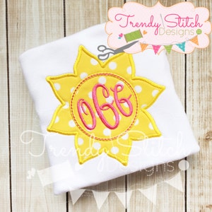 Könnte beinhalten: Ein weißes T-Shirt mit einem gelben Sonnen-Applikationen mit weißen Punkten und einem rosafarbenen Monogramm in einem Kreis. Das Monogramm lautet "OGG".