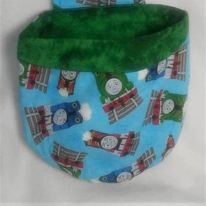 May include: A blue and green fabric storage bin with a Thomas the Tank Engine print. The bin has a flap on the top that can be folded down.