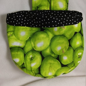 May include: A green apple print fabric storage bin with a black and white polka dot trim. The bin has a strap for hanging.