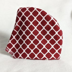 Puede incluir: Una mascarilla facial de tela roja con un patrón geométrico blanco. La mascarilla está hecha de un material suave y transpirable y tiene una forma contorneada para un ajuste cómodo.
