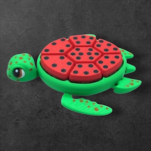 May include: A green turtle toy with a red and black watermelon shell. The turtle has brown spots and a cute face.