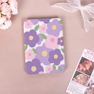 May include: A rectangular protective tablet case featuring a repeating pattern of stylized flowers in shades of purple, light pink, and yellow with small green leaves on a white background. The case has rounded corners and a smooth, glossy finish.