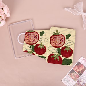 May include: A clear phone case and a patterned phone case featuring a tomato design. The tomato design includes red tomatoes with green plaid accents on a lined, cream-colored background. The phone case is a food-themed accessory.