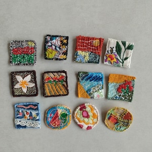 Peut inclure: Une collection de douze patchs en tissu faits à la main avec des motifs brodés. Les patchs présentent divers motifs colorés, notamment des scènes florales, abstraites et de paysages. Les formes sont carrées et rondes, présentant une variété de textures et de couleurs.
