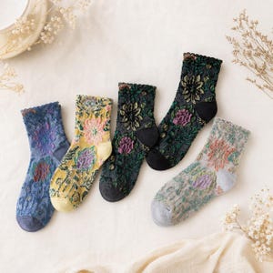 May include: Five pairs of ankle socks featuring intricate floral lace patterns in blue, yellow, dark green, black, and light gray. Each pair has a scalloped cuff, a solid-colored heel and toe section, and a textured, semi-sheer knit construction.