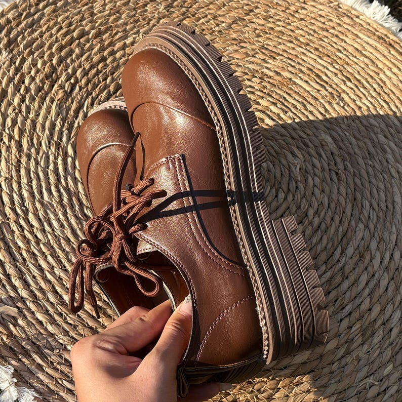 May include: Brown leather oxford shoes with thick, ridged soles. The shoes have a classic lace-up design and are made of a smooth, polished leather. The soles are approximately 1.5 inches thick.