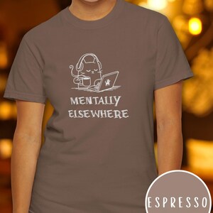 May include: Espresso-colored t-shirt featuring a white graphic of a cat wearing headphones, holding a coffee cup, and using a laptop. The text "MENTALLY ELSEWHERE" is below the graphic. A circular color swatch reads "ESPRESSO".