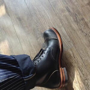 May include: Black leather boots with a brown leather sole and laces. The boots are worn with a pair of blue and white striped pants.