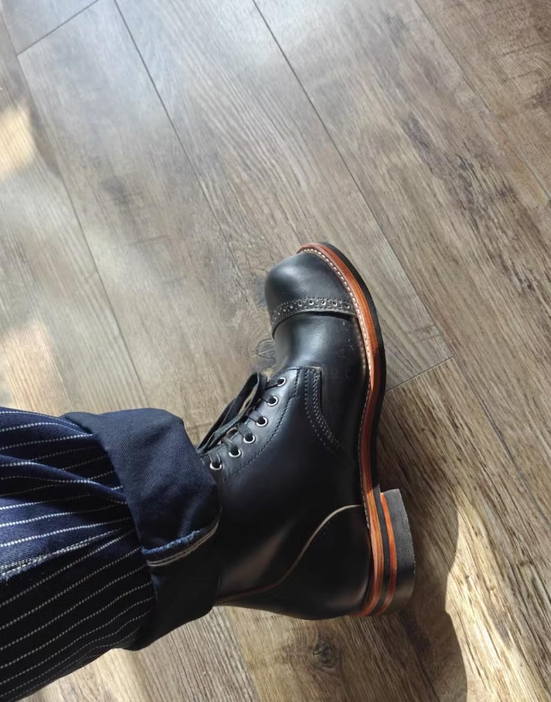 May include: Black leather boots with a brown leather sole and laces. The boots are worn with a pair of blue and white striped pants.