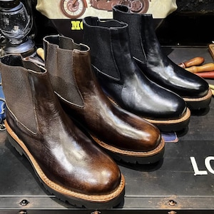 Puede incluir: Cuatro pares de botines Chelsea de cuero en varios tonos de marrón y negro. Los botines tienen paneles laterales elásticos y suelas gruesas con un ribete marrón claro. Los botines están dispuestos en fila, mostrando sus diferentes colores y estilos.