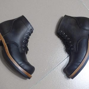May include: A pair of black leather boots with brown leather soles. The boots have a lace-up closure and a rounded toe.
