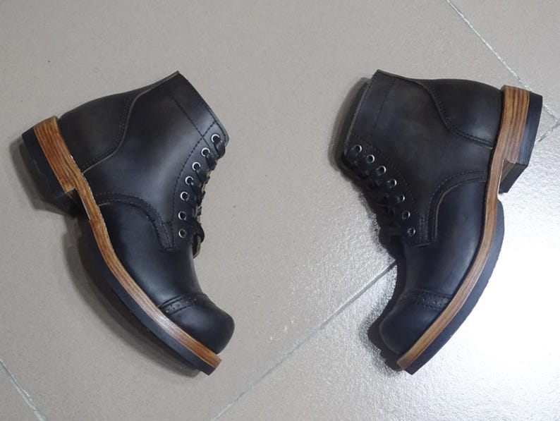 May include: A pair of black leather boots with brown leather soles. The boots have a lace-up closure and a rounded toe.