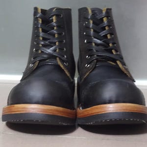 May include: A pair of black leather boots with brown soles and laces. The boots have a classic work boot style.