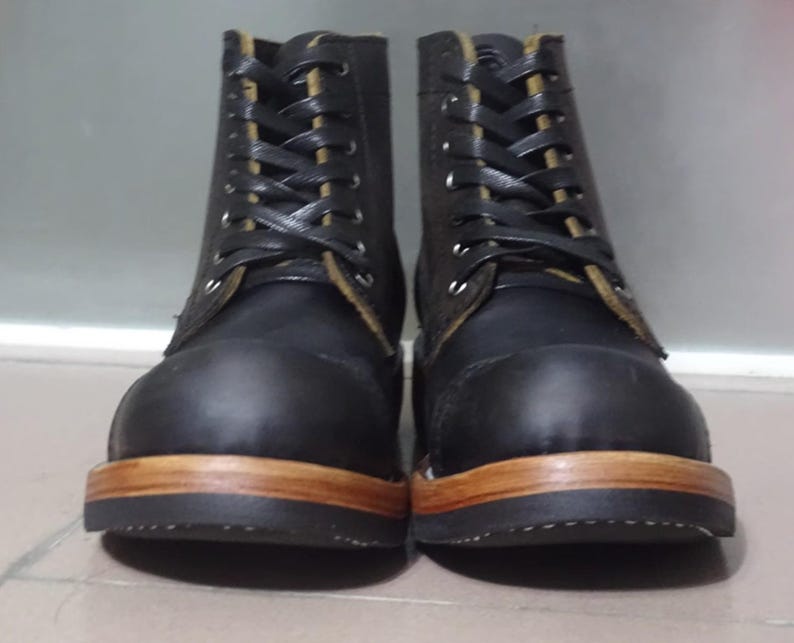 May include: A pair of black leather boots with brown soles and laces. The boots have a classic work boot style.