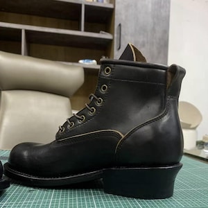Op de afbeelding: Een zwarte leren werklaars met vetersluiting. De laars heeft een ronde neus, een stevige hak en metalen veterogen. Het leer heeft een licht versleten uiterlijk, wat duidt op duurzaamheid en gebruik.