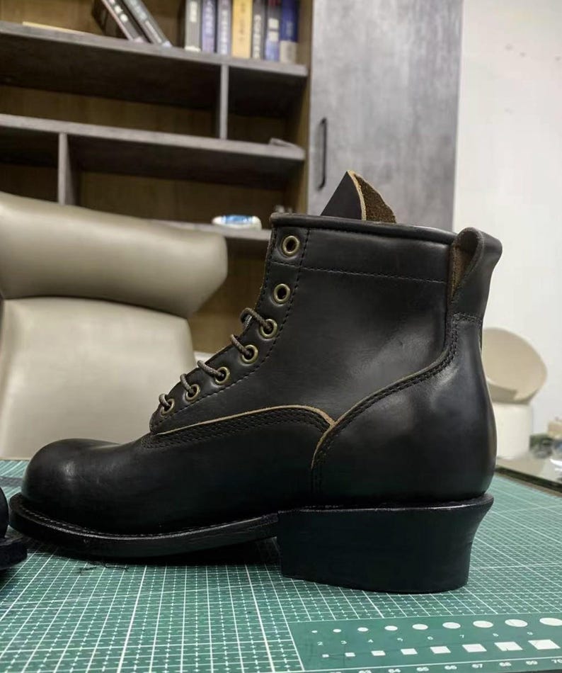 Op de afbeelding: Een zwarte leren werklaars met vetersluiting. De laars heeft een ronde neus, een stevige hak en metalen veterogen. Het leer heeft een licht versleten uiterlijk, wat duidt op duurzaamheid en gebruik.