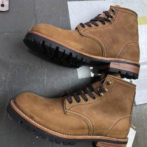 May include: Two brown leather work boots with black lug soles and brown laces. The boots have a classic design with visible stitching and metal eyelets. The soles are thick and durable, suitable for rugged use. The boots are new and unworn.
