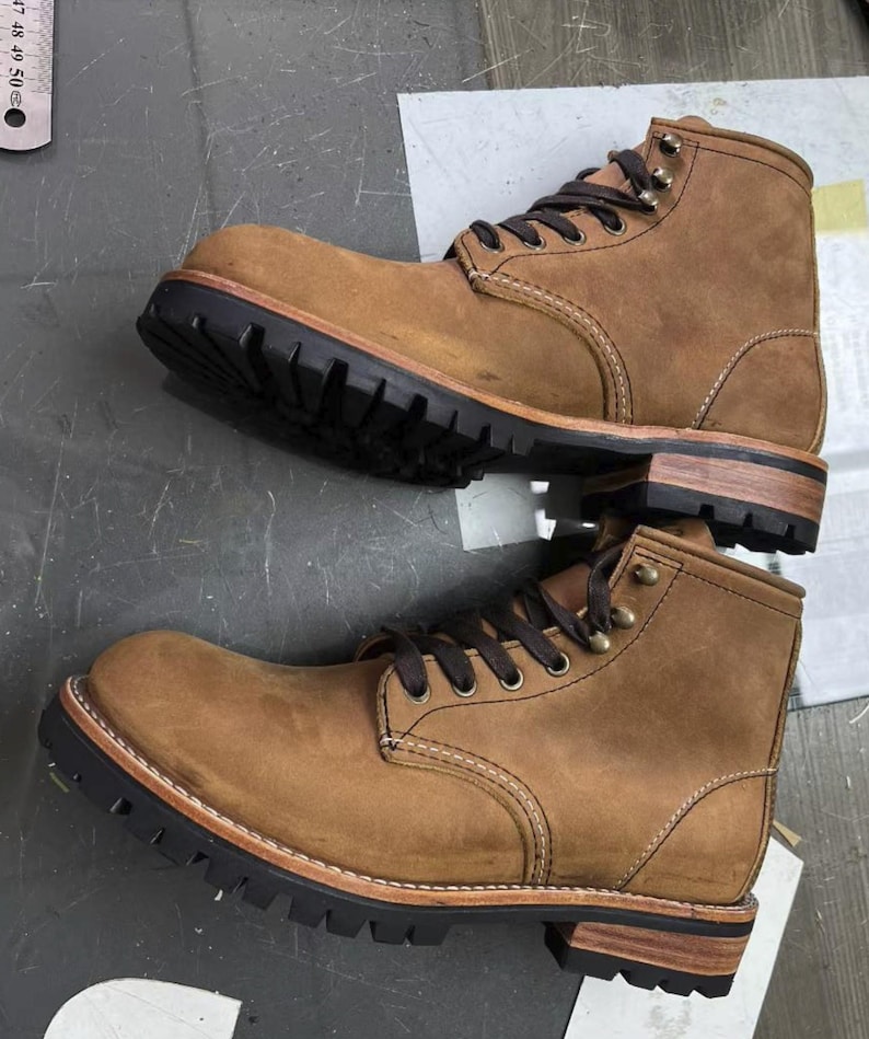 May include: Two brown leather work boots with black lug soles and brown laces. The boots have a classic design with visible stitching and metal eyelets. The soles are thick and durable, suitable for rugged use. The boots are new and unworn.