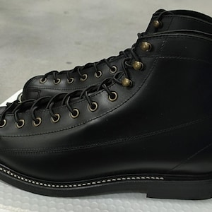 May include: Black leather work boots with a high-top design. The boots feature a lace-up closure with brass eyelets and a stitched sole. The boots are new and unworn.