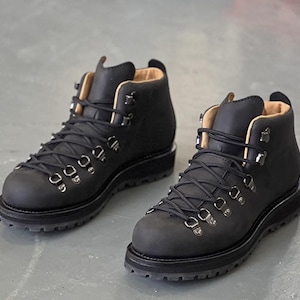 May include: A pair of black leather hiking boots with metal eyelets and black laces. The boots have a padded collar and a thick, lugged sole. The interior lining is tan. These sturdy boots are designed for outdoor activities and rugged terrain.