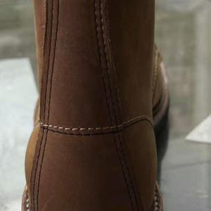 May include: A brown leather work boot with a rounded toe and a sturdy sole. The boot features visible stitching and a padded collar. The heel is approximately 1.5 inches high. The boot is designed for durability and rugged use.