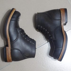 May include: A pair of black leather lace-up boots with brown leather soles. The boots have a rugged look and are made of high-quality materials.