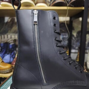 May include: Black leather boot with a side zipper and lace-up closure. The boot features a pull tab at the top and a sturdy sole. Other boots are visible in the background.