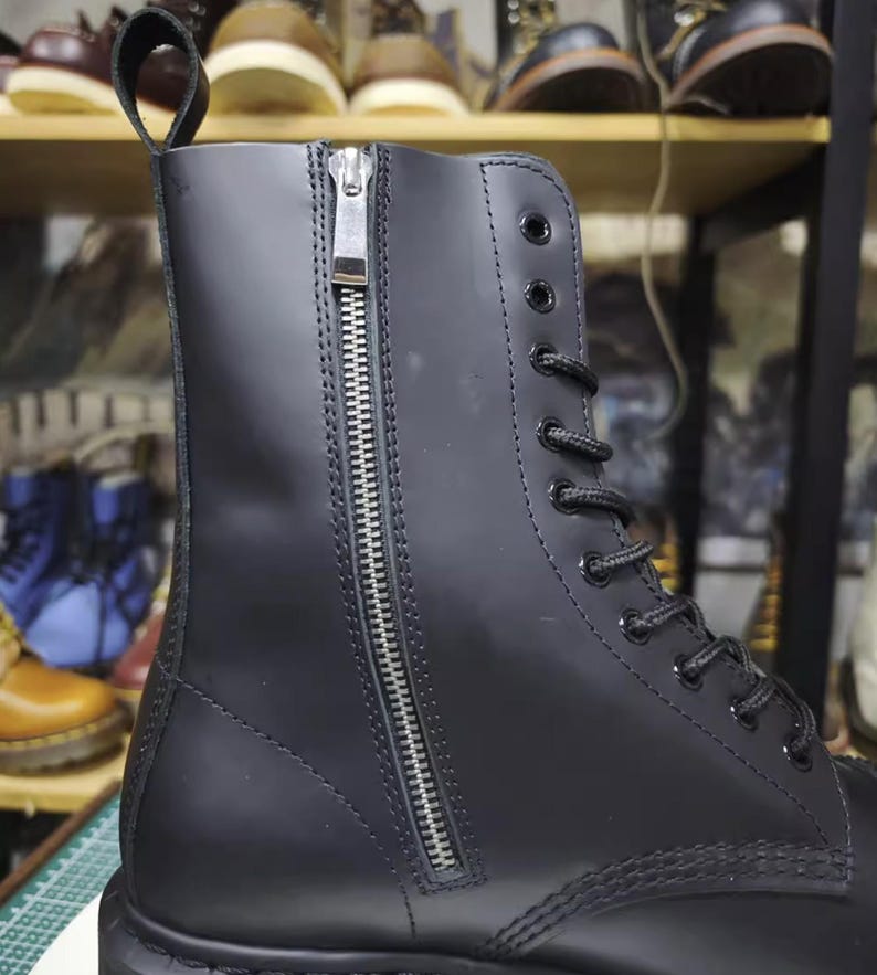 May include: Black leather boot with a side zipper and lace-up closure. The boot features a pull tab at the top and a sturdy sole. Other boots are visible in the background.