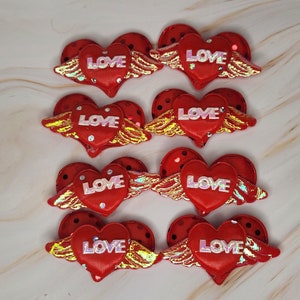May include: Eight red felt heart-shaped embellishments with gold wings and the word "LOVE" in white lettering. Each heart has a red polka dot pattern.