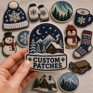 May include: A collection of embroidered winter-themed patches including a snow globe shape with the text CUSTOM PATCHES, a beanie, mittens, a mug, a snowman, a penguin, a sock, a sled, and mountain landscapes in blue, white, and red.