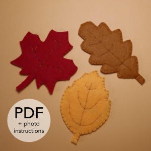Può includere: Tre ritagli di foglie di feltro nei colori autunnali: rosso, marrone e giallo. Ogni foglia ha dettagli di venature cucite. L'immagine include il testo "PDF + istruzioni fotografiche".
