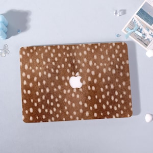 May include: A brown laptop skin with a white spotted pattern, resembling deer fur. The Apple logo is visible in the centre. The skin is rectangular and covers the top of the laptop.