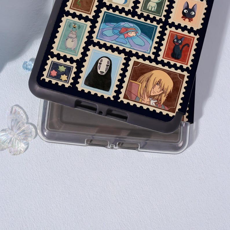 Puede incluir: Una funda de tel&eacute;fono negra con un collage de coloridos dise&ntilde;os de sellos postales. Los sellos representan varios personajes y escenas de anime, incluyendo un gato negro, una ni&ntilde;a con un vestido azul y un personaje con pelo largo y rubio. La funda es de pl&aacute;stico resistente.